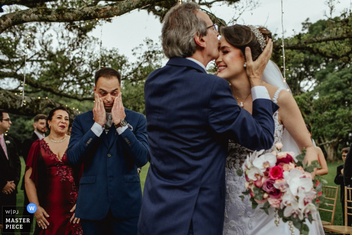 Groom thrilled to see the father of the bride kissing her at the outdoor ceremony Groom thrilled to see the father of the bride kissing her at the ceremony - Alto da Capela