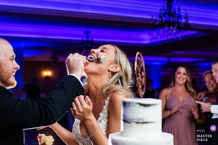 Photo by: <a href="https://www.wpja.com/contests/2019-v18/best-wedding-photographers/2566614">Michelle Arlotta - Milford New Jersey</a> Groom smears cake on bride's face as people watch on at Bear Brook Valley NJ wedding
