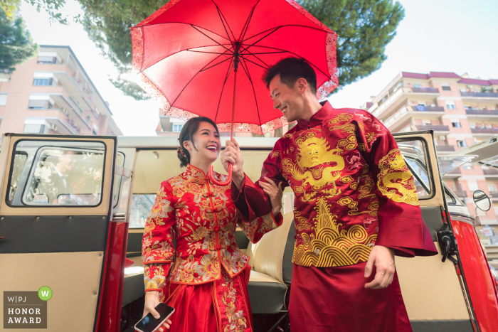 Photographie de mariage à Rome, Italie: le couple descendait de la camionnette avec une robe de mariée traditionnelle et tenait le parapluie rouge.