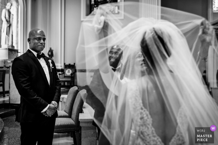 Photo by: <a href="https://www.wpja.com/contests/2019-v18/best-wedding-photographers/2567692">JD Land - Marlton New Jersey</a> New Jersey Wedding Ceremony Photographer: Groom and best man looking on as the mother of the bride removes the brides veil