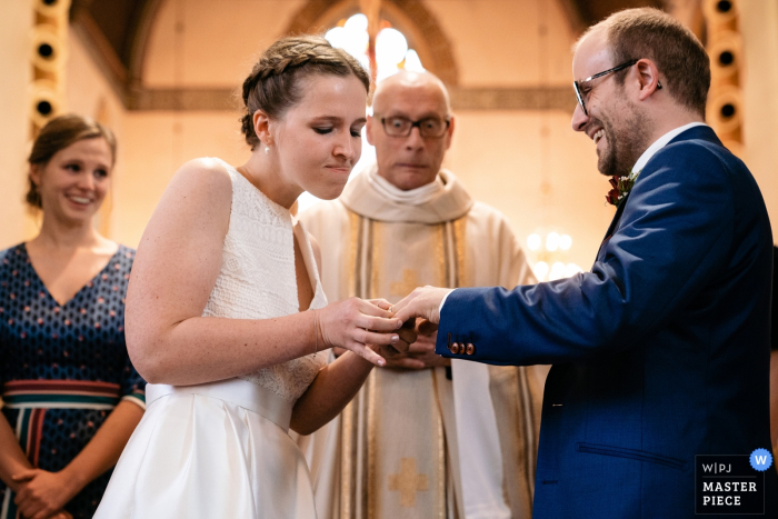 Photo by: <a href="https://www.wpja.com/contests/2019-v18/best-wedding-photographers/2567858">Yves Schepers - Bonheiden Antwerpen</a> Antwerpen Wedding Ceremony Photographer: Bride struggles to get the ring around her groom's finger, the priest is startled about her brusque method