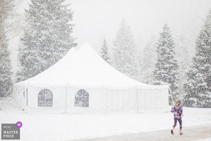 A bridesmaid sprints through dumping snow Victor, Idaho wedding image contains: A bridesmaid sprints through dumping snow