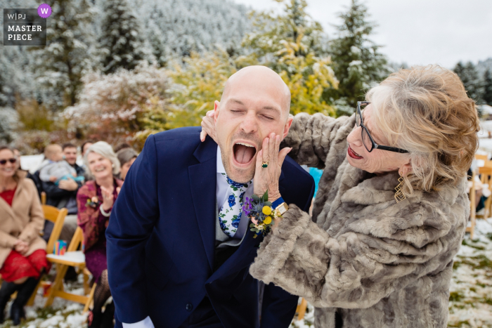 Wedding photography in the snow at Victor, Idaho | The mother of groom wipes lipstick off him after kissing at front of aisle