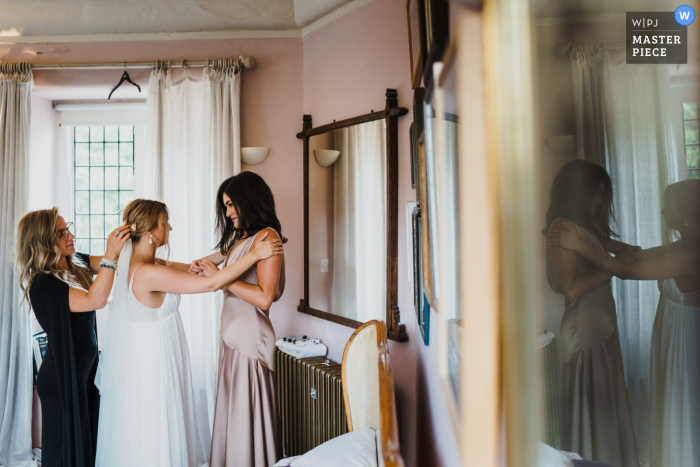 Voewood, Norfolk, Reino Unido - reportagem de casamento | Noiva e dama de honra compartilham um momento durante os retoques no preparo das noivas