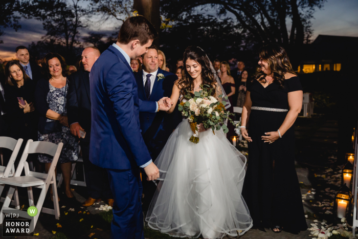 Foto di cerimonia di matrimonio all'aperto del Three Village Inn, NY: La sposa camminava lungo il corridoio con i genitori. Lo sposo le prese la mano.