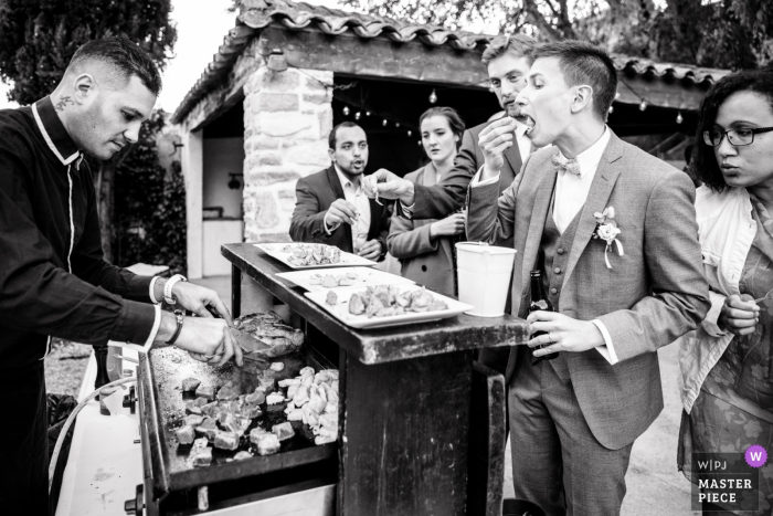 Photo by: <a href="https://www.wpja.com/contests/2019-v19/best-wedding-photographers/2571189">Ludovic Lieffrig - Saint-Mathieu-de-Tréviers </a> Domaine des Rives wedding reception image of the groom enjoying some snacks from the grill.