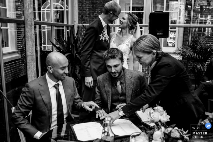 Photo by: <a href="https://www.wpja.com/contests/2019-v19/best-wedding-photographers/2571534">Linda Bouritius - Amersfoort Utrecht</a> Amsterdam, The Netherlands wedding image: While the best men is signing the wedding contract the bride and groom only have eye for each other
