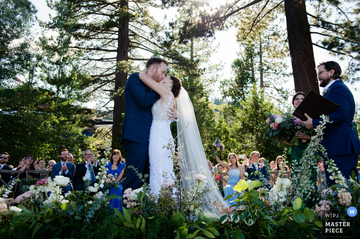 West Shore Cafe, Lake Tahoe CA Fotógrafo de bodas: El beso de los novios al final de la ceremonia al aire libre bajo los árboles.