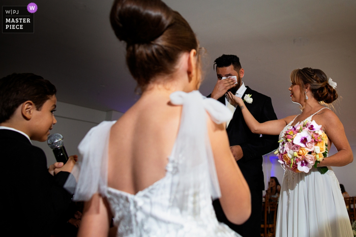 Photo by: <a href="https://www.wpja.com/contests/2019-v19/best-wedding-photographers/2571885">Claudia Amorim - Goiânia Goias</a> Favo de Mel wedding ceremony image of the groom becoming emotional as a young man speaks on a microphone