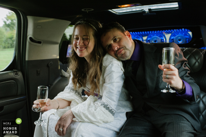 A bride and groom snuggle while holding champagne glasses Wedding photo In a Limo in Altamont, NY - A bride and groom snuggle while holding champagne glasses as they ride in a limo to their reception.