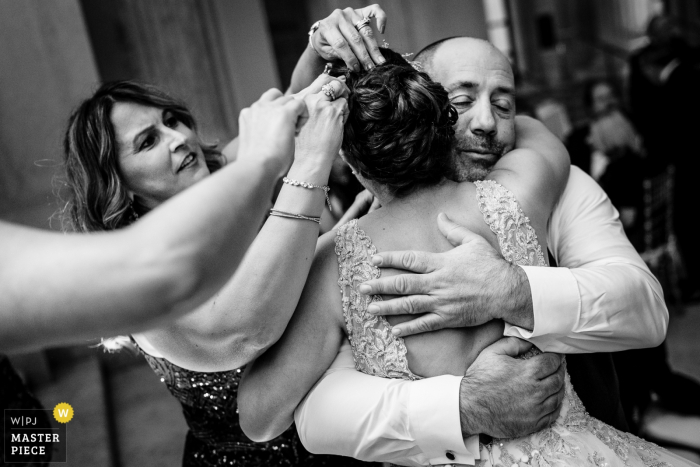 Receptie Locatie Fotografie | De bruid maakt haar rondes bij de receptie. Ze knuffelt haar oom terwijl haar tantes bezig zijn haar haar te repareren.