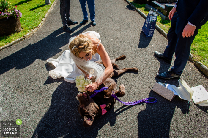 Munster trouwfoto van buiten de kerk - bruid speelt met haar hond na haar huwelijksceremonie