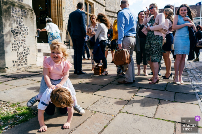 Reportage de mariage au bureau d'enregistrement de Winchester | Une petite fille chevauchant son frère pendant que les invités quittent le lieu de la cérémonie