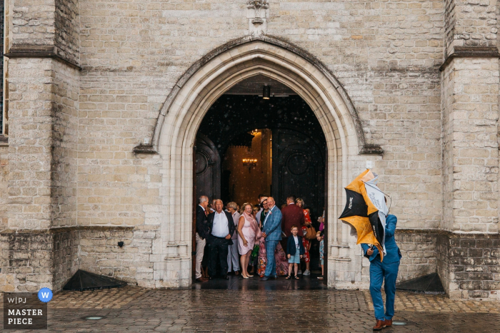 Antwerpen kerkelijke huwelijksfotografie | Iedereen had al onderdak in de kerk toen het plotseling begon te gieten, slechts 1 man worstelde met het sluiten van zijn paraplu vanwege de zware wind.