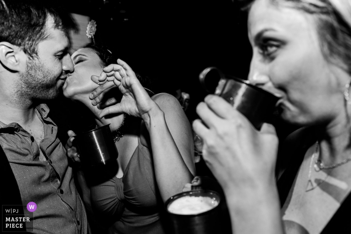 Foto del ricevimento di matrimonio in Brasile di una coppia che si bacia e uno spettatore che beve in primo piano