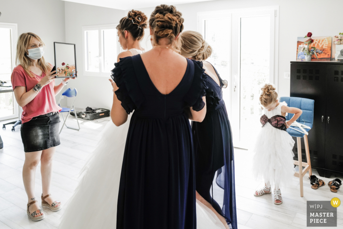 Photographe de mariage français | la fille de la mariée joue avec le soutien-gorge de sa mère en enfilant la robe de mariée