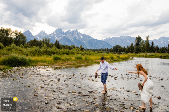 Imagem do dia do casamento do Parque Nacional de Grand Teton da noiva e do noivo cruzando um riacho