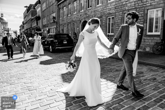 Fotografía de boda de Canadá desde el Viejo Montreal de la pareja caminando de la mano mientras los invitados los siguen en la calle