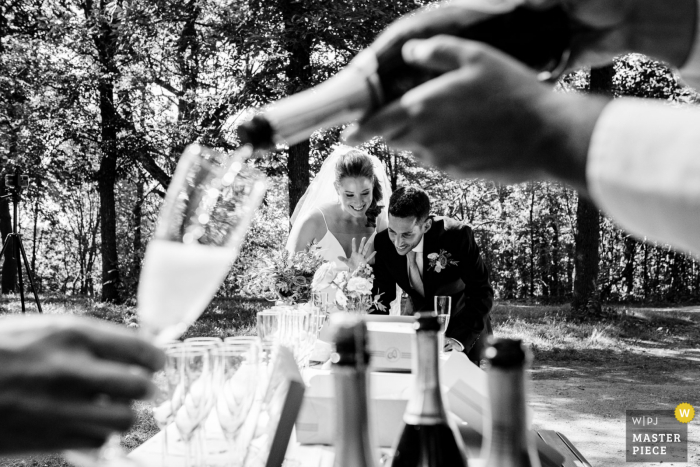 Quebec Canada wedding photo at Parc Mont Royal, Montreal of a Wedding couple chatting with zoom guests on laptop while a server pours prosecco into a guest's glass 