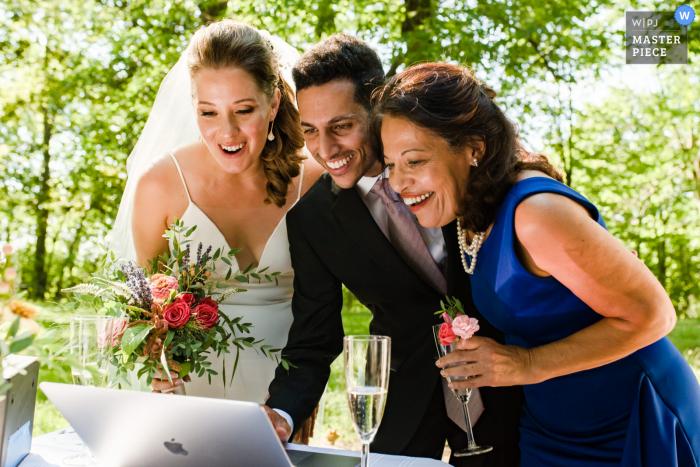 Fotografia di matrimonio all'aperto in Quebec dal Parc du Mont Royal, Montreal degli sposi e della madre dello sposo che chiacchierano con gli ospiti che hanno partecipato al matrimonio online