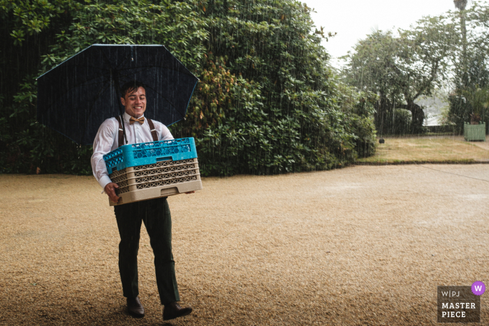 Fotografia de casamento na Bretanha em um local de recepção em Morbihan. Surpreso com a tempestade, o goom ajuda a trazer sorvete de coquetel para dentro sob a chuva forte