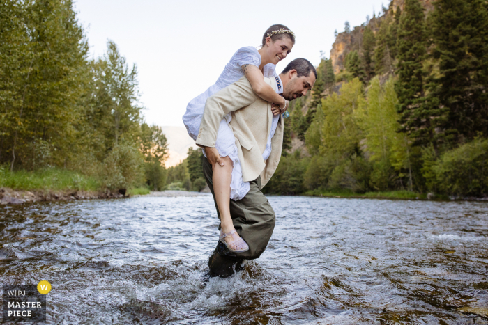 Foto de la fuga de bodas de MT de Rock Creek, Montana, mientras el novio lleva a la novia a través del agua a la ceremonia