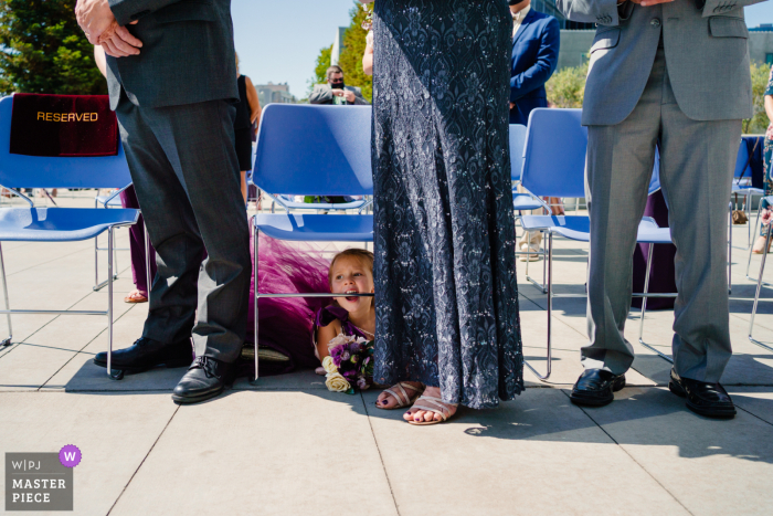 The Cathedral of Christ the Light Outdoor Ceremony image of flower girl biting chair during ceremony The Cathedral of Christ the Light Outdoor Ceremony image of flower girl biting chair during ceremony