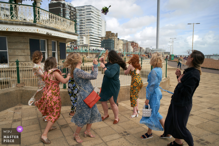 s Brighton Bandstand, Brighton Bride throws her bouquet above and beyong the waiting friends in this wedding day image Brighton Bandstand, Brighton | Bride throws her bouquet above and beyong the waiting friends