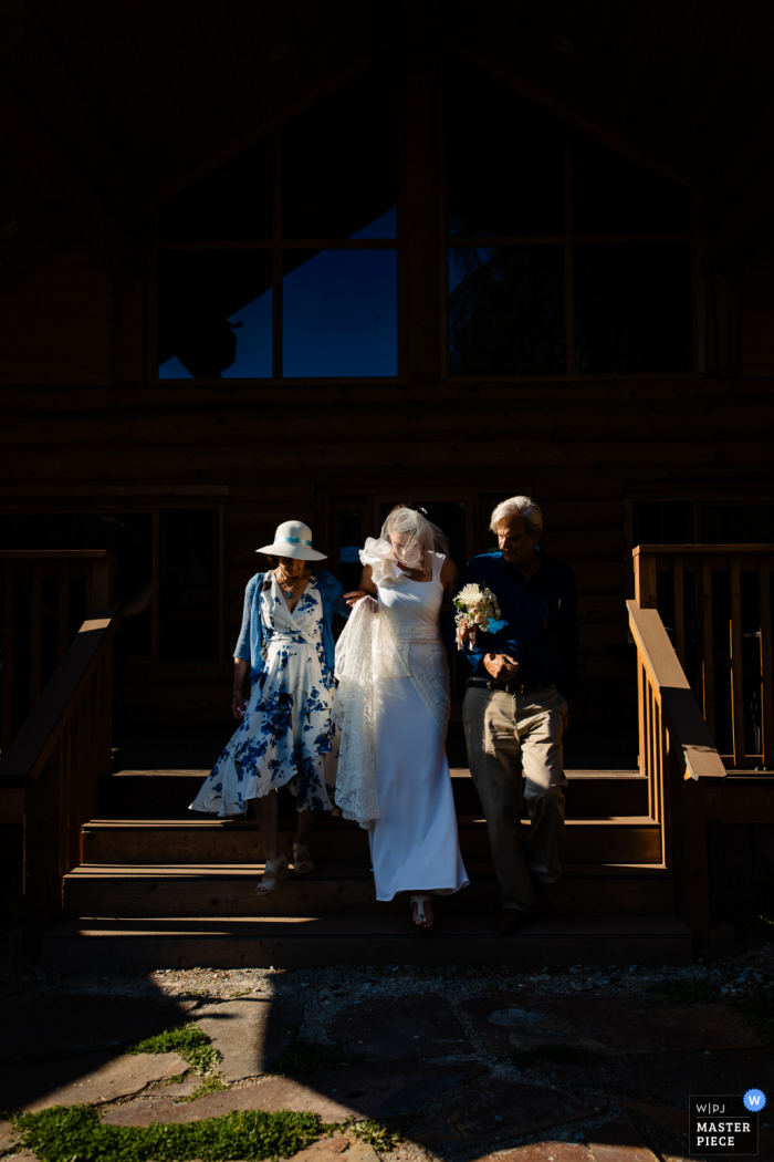 Fotografía de boda de Lochsa Lodge, Idaho, mostrando a la novia caminando por el pasillo con madre y padre