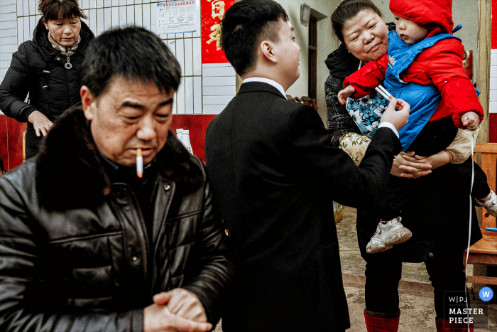 Fotografia di matrimonio in Cina da Chengdu Sichuan a casa della sposa dello sposo che scherza con un bambino, sta prendendo una sigaretta per il bambino