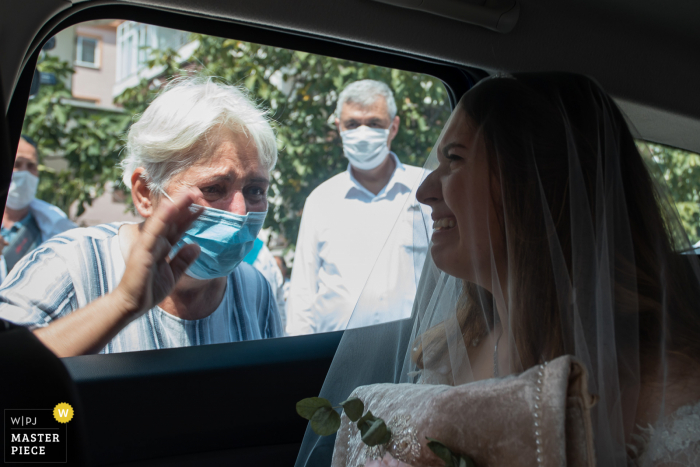 Luleburgaz Trouwfotografie | Bruid huilt in de auto terwijl het oude familielid met een covid-19-masker haar gedag zwaait buiten het raam