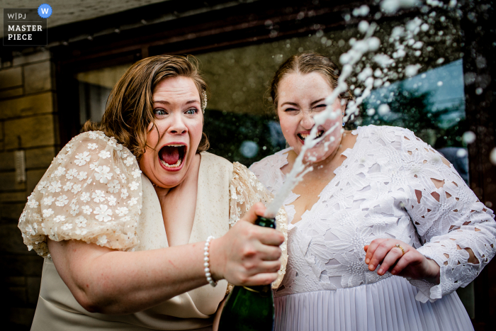 Brides react to a bottle of champagne spraying at their backyard wedding in New Lenox, IL