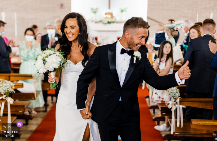 IE wedding reportage photo from Blackrock Co Dublin Ireland of the Bride and Groom defeating the covid odds and get married with Pure joy on their faces walking down the aisle