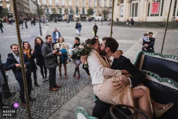 Fotografía de boda de Rennes, Francia, de los novios en un carrusel frente a los invitados.