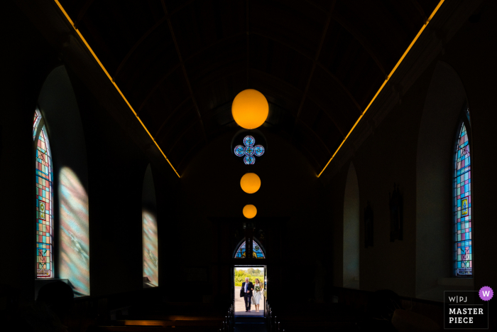 trouwfoto uit Virginia, Ierland waarop de bruid en vader te zien zijn die in groot licht aankomen in een bijna lege landelijke kerk voor een bruiloft voor 14 personen