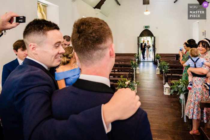 Foto de reportaje de boda de IE del BrookLodge Hotel, Wicklow, Irlanda que muestra todos los ojos puestos en el novio cuando la novia y el papá llegan a la ceremonia