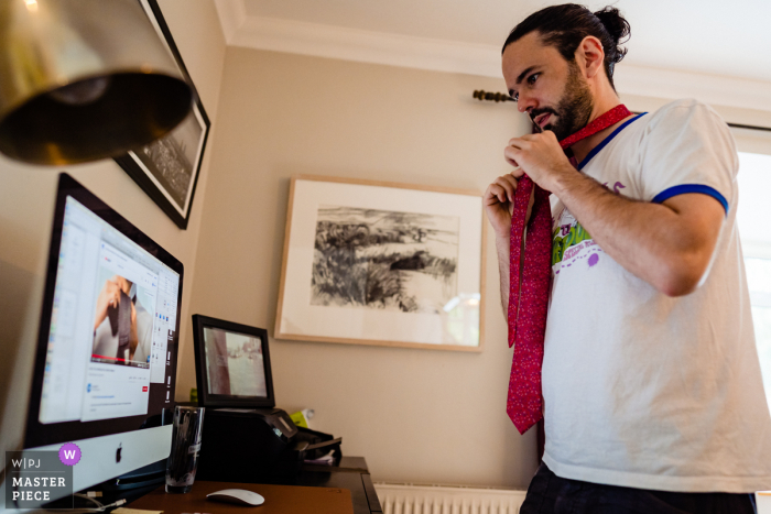 Sto preparando la foto del matrimonio dalla casa dello sposo di Horetown che lavora la cravatta con l'aiuto del suo computer portatile