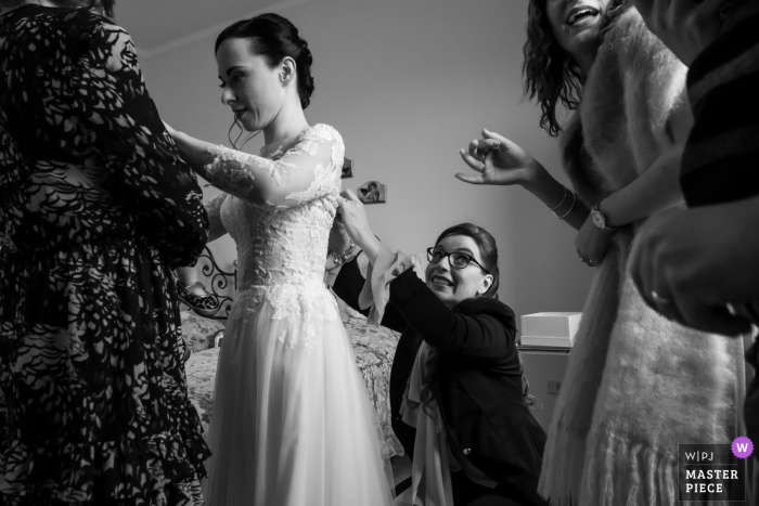 Mantova, Italy Wedding Photo | While the bride is assisting her sister, the friend who fastens the dress looks in vain for help to solve a sudden problem of closing the dress