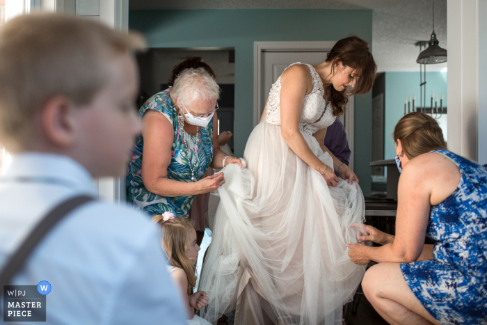 Kanada Hochzeitsfotografie von einer Hinterhofhochzeit im Freien in Ayr, Ontario, Kanada zeigt Die Braut, Mutter der Braut, Brautjungfern pflücken alle Kiefernnadeln aus ihrem Kleid, das die Braut während der Porträtsitzung angesammelt hat