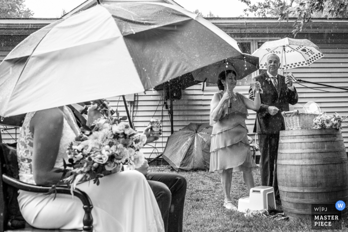 Fotografía de boda al aire libre desde una ceremonia en el patio trasero en St. Thomas, Ontario, Canadá, mostrando los discursos continúan durante un aguacero con sombrillas