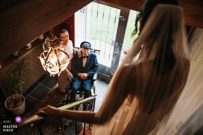 Belgium Wedding Photographer | The parents of the bride (and her palliative dad) watch their daughter come down the stairs on her wedding day