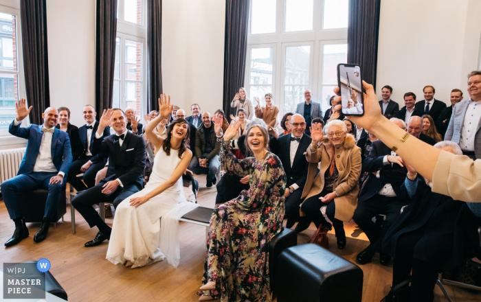 Fotografia di matrimonio in Belgio | Il padre palliativo della sposa saluta e guarda sua figlia che si sposa in municipio attraverso un ipad