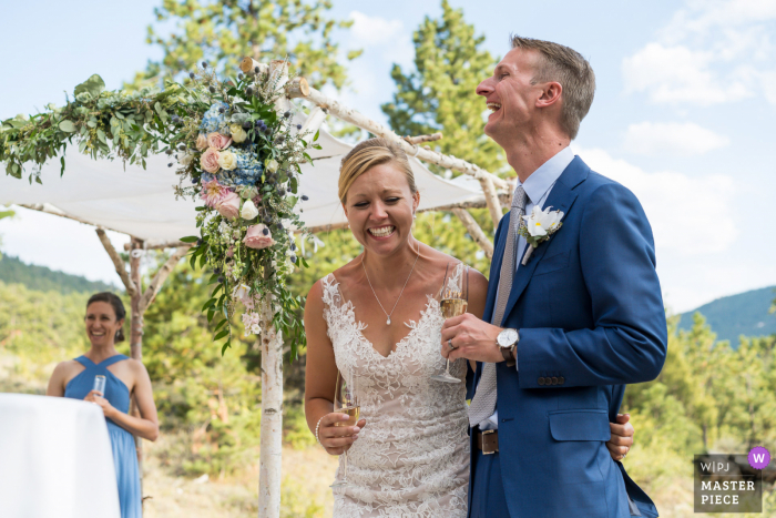 foto de boda de la ceremonia al aire libre en Estes Park, CO de la pareja riendo durante los brindis