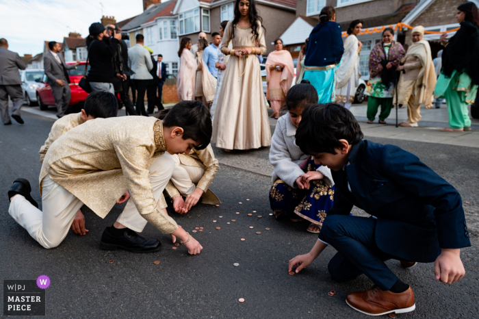 huwelijksfotografie uit Londen, VK van kinderen die kleingeld ophalen na de Aziatische huwelijksceremonie