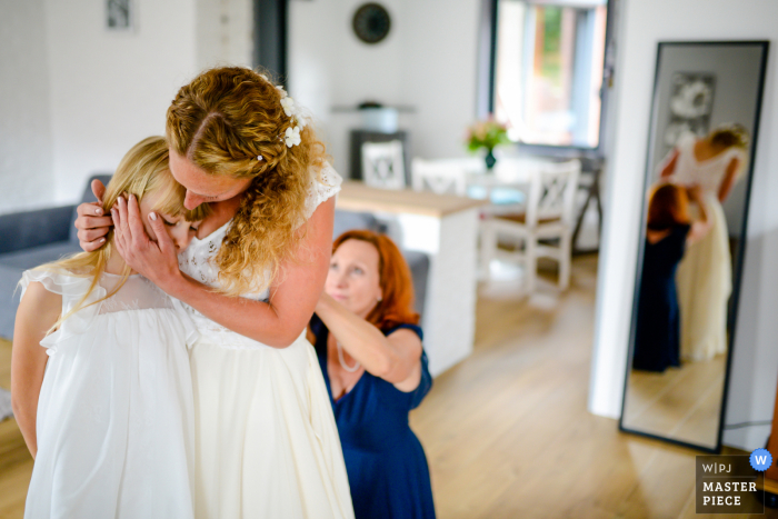 Eine Hauts-de-France-Braut beruhigt ihre Tochter, während ihre Mutter ihr Hochzeitskleid schließt