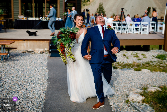 De bruidegom lacht terwijl hij met zijn nieuwe vrouw het eiland afloopt na hun buitenceremonie in Arapahoe Basin, CO