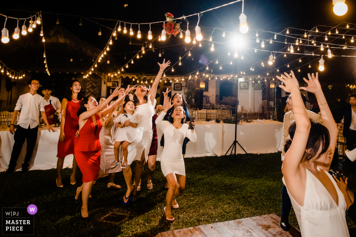 Fotografía de boda de Vietnam en la recepción de la novia lanzando el ramo a sus invitados solteros