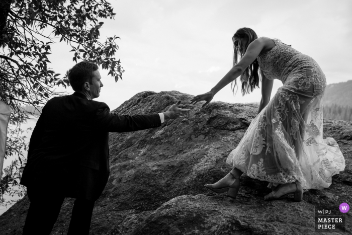 Image of the The groom helping his bride down from the location they chose to read their vows and self marry during their elopement in Wyoming