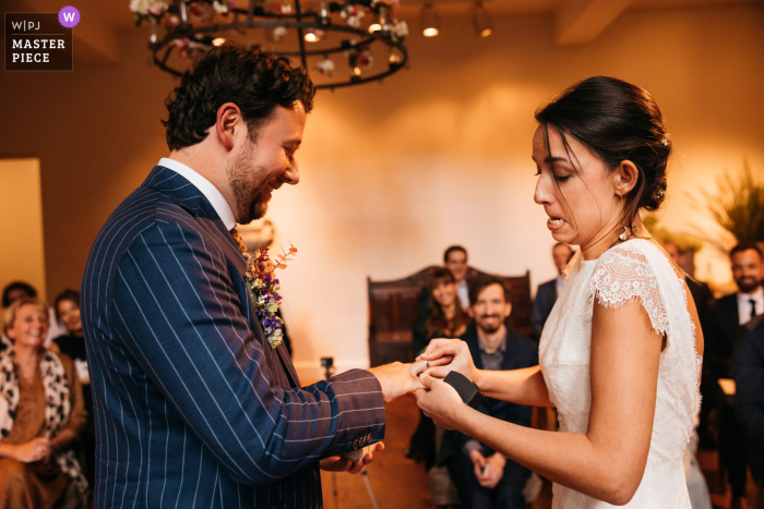 De bruid trekt gezichten terwijl ze tijdens deze Belgische ceremonie de gezwollen vinger van haar man probeert te bellen