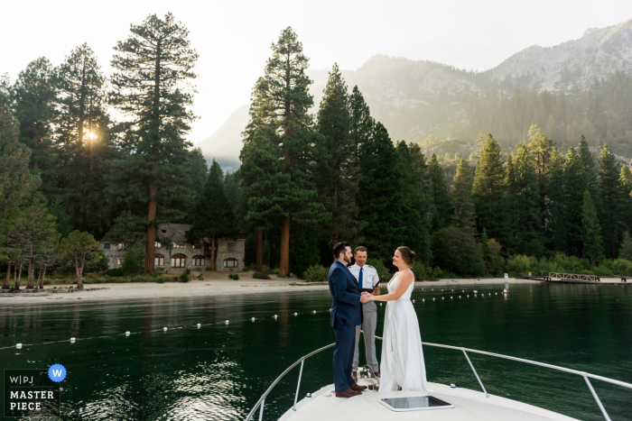 Een bruid en bruidegom lopen weg op de boeg van een Lake Tahoe Boat Rides-charterboot, onder leiding van de kapitein, onder de toppen van Emerald Bay en starend naar Vikingsholm Castle